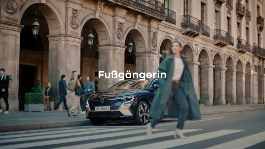 Eine Fußgängerin geht schnell über einen Zebrastreifen. Hinter ihr steht direkt vor dem Zebrastreifen Ihr Renault.